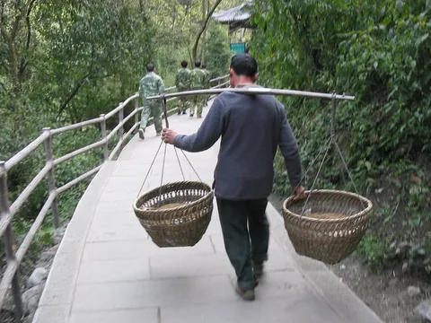 Porter with a shoulder pole on a mountain path, China — Nicolas Marincic