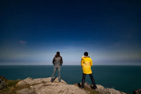 Two stargazers on coastal rocks at blue hour, France — Nicolas Marincic