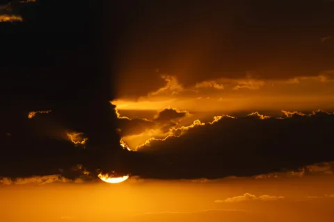 Eclipsed crescent sun setting behind clouds, France — Nicolas Marincic