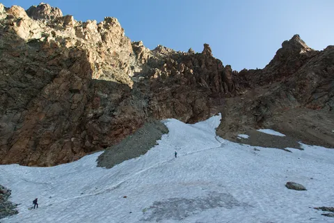 Climbers crossing a snowfield below red rock towers, Italy — Nicolas Marincic