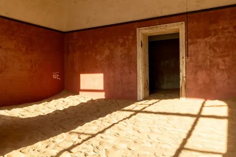 Sand-filled red room in window light, Kolmanskop, Namibia — Nicolas Marincic