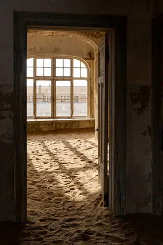 Dark doorframe onto a sunlit sandy room, Kolmanskop, Namibia — Nicolas Marincic