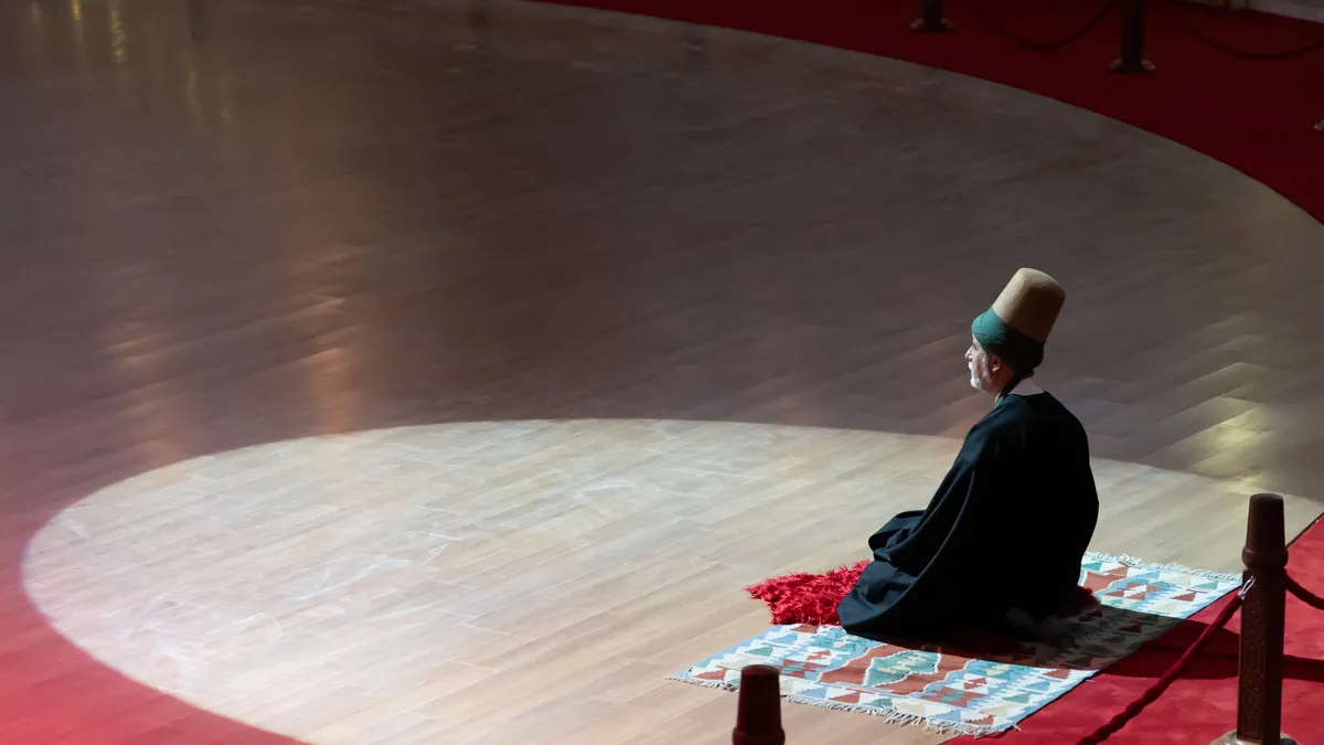 Mevlevi dervish kneeling in light before the Sema, Konya, Turkey — Nicolas Marincic