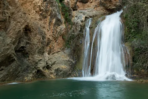 Cascade dans un bassin émeraude sous une falaise ocre, France — Nicolas Marincic