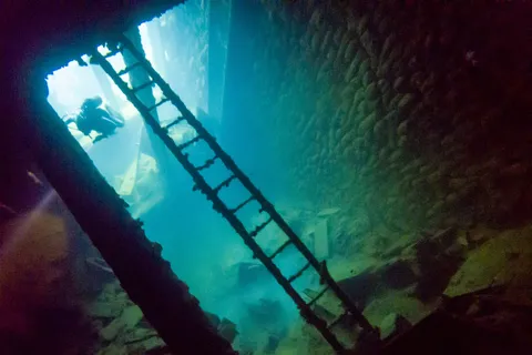 Diver above an interior ladder in a shaft of light, Umbria wreck, Sudan — Nicolas Marincic