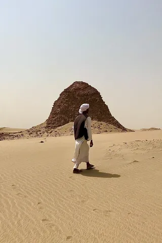 Man in a jalabiya walking towards a pyramid at Nuri, Sudan — Nicolas Marincic