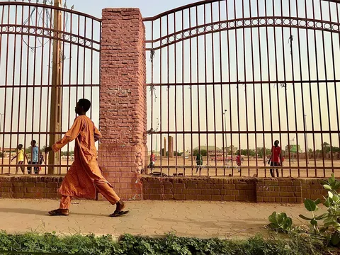 Man in an orange jalabiya walking past a gate, Khartoum, Sudan — Nicolas Marincic