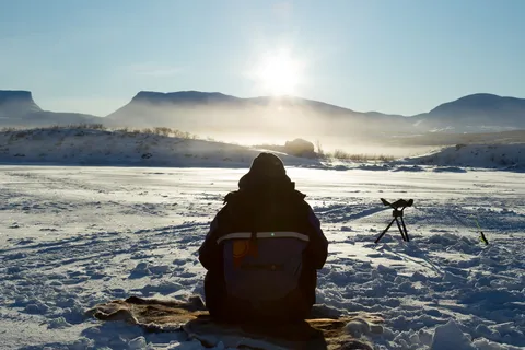 Ice fisher against the low sun, Torneträsk, Sweden — Nicolas Marincic